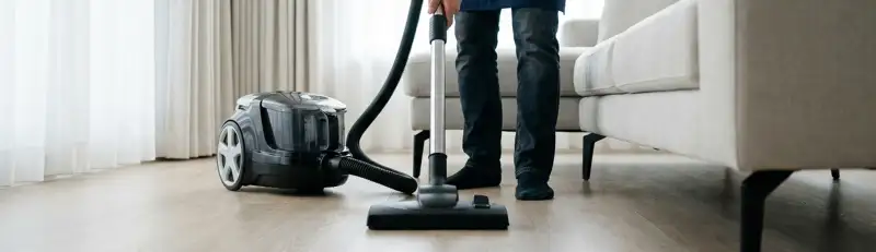 Professional house cleaner vacuuming a living room floor with a canister vacuum cleaner, Sarasota, FL.