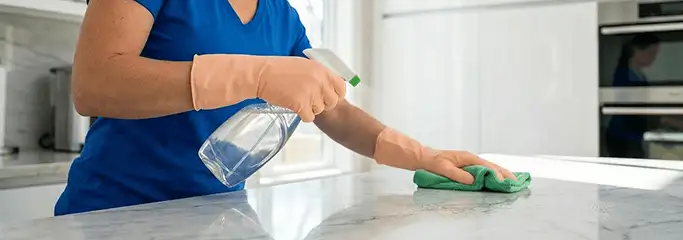 Maid service worker spraying and wiping a kitchen countertop with a microfiber cloth for sanitizing, Sarasota, FL.