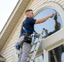 Professional window cleaner on a ladder using a squeegee to clean an exterior arched window, Sarasota, FL.