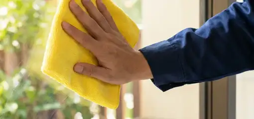 House cleaner wiping a glass window with a yellow microfiber cloth for streak-free cleaning, Sarasota, FL.